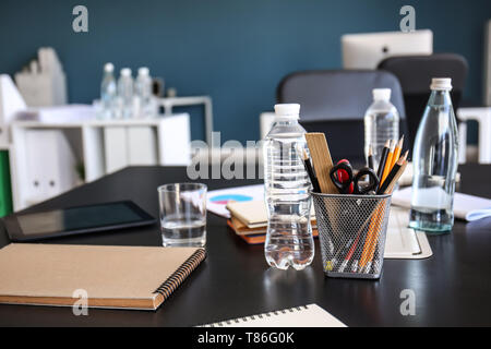 Tavolo con materiale di cancelleria e bottiglie di acqua preparata per business meeting nella sala conferenze Foto Stock