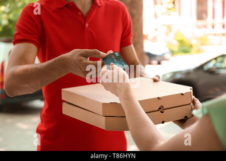 Giovane donna di pagare per la pizza con carta di credito alla porta. Il cibo del servizio di consegna Foto Stock