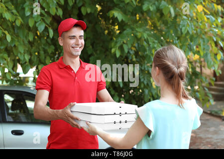 Giovane uomo dando scatole per pizza a donna all'esterno. Il cibo del servizio di consegna Foto Stock