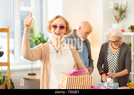 Gioiosa di età della donna in possesso di una scatola presente nelle sue mani Foto Stock