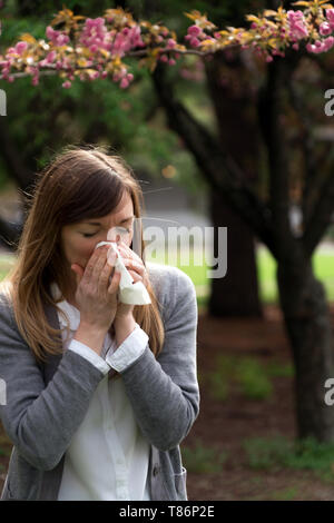 Donna millenario starnuti nel parco circondato da fiori - sembra che le allergie! Foto Stock