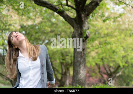 Una millenaria donna seduta in un parco godendo il momento completamente in pace con il mondo e felice della vita Foto Stock