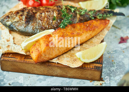 Grigliata di pesce dorado e bistecca di salmone su una tavola di legno con verdure carta kraft su sfondo grigio Foto Stock