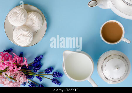 Latte, meringhe di bianco, latte jar pastello su sfondo blu decorato con muscari e fiori di giacinto. Top down, piatto laici. Prima colazione e tempo di caffè Foto Stock