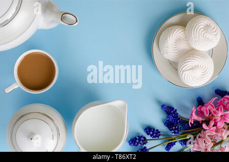 Latte, meringhe di bianco, latte jar pastello su sfondo blu decorato con muscari e fiori di giacinto. Top down, piatto laici. Prima colazione e tempo di caffè Foto Stock