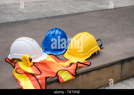 Bianco, blu, giallo hard casco di sicurezza sul corpetto con nastro di misurazione per ingegnere e lavoratore Foto Stock