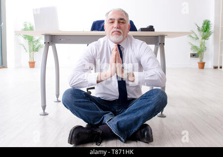 Imprenditore invecchiato facendo esercizi yoga in ufficio Foto Stock