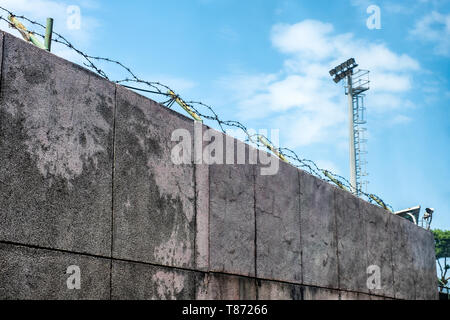 Muro di pietra con bobine di filo spinato e videocamera di sicurezza in carcere Foto Stock