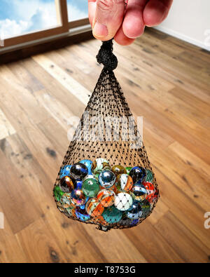 Maschio lato tenendo un sacchetto di marmi policromi contro marrone pavimento in legno duro Foto Stock