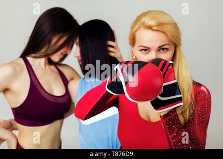 Montare la giovane donna in posa di guantoni da pugilato sullo sfondo di due ragazze sportivo. avversari. desiderio di vincere Foto Stock