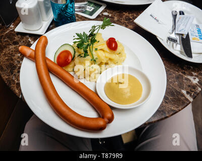 Francoforte, Germania - Apr 29, 2019: POV alla piastra con due tradizionali lungo tedesco salsicce e patate con insalata di verdure e piastra di senape Foto Stock