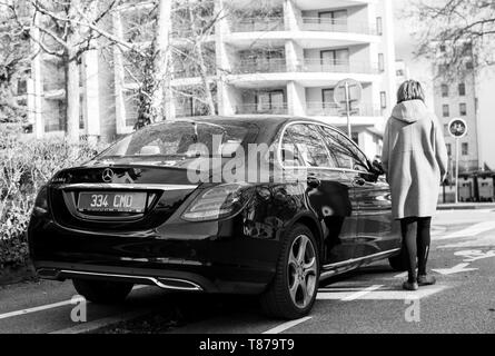 Strasburgo, Francia - Feb 23, 2017: Donna che cammina verso il lusso di Mercedes-Benz E220d diesel auto parcheggiata su una strada tranquilla nella città francese in bianco e nero Foto Stock