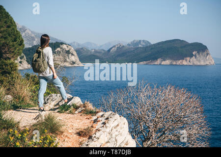 Un turista con lo zaino sulla cima di una scogliera o collina vicino al mare appare in lontananza. Viaggiare da soli. Foto Stock