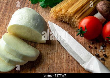 Su una tavola di legno laici a fette di mozzarella accanto a lei il coltello sul lato destro sale marino con pepe rosso e nero, sopra i pomodori ciliegia, funghi, materie Foto Stock