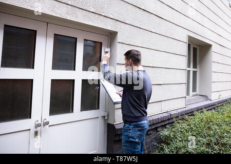 Giovane uomo servizio esaminando porta chiusa all'ingresso Foto Stock