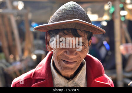 Basar, Arunachal Pradesh, India - 10 gennaio 2019: Ritratto Galo Tribal vecchio uomo vestito con il tradizionale cappello di bambù, in background mercato. Foto Stock