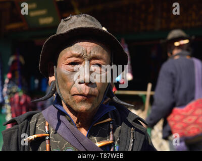 LONGWA, Nagaland, India - 15 gennaio 2019: Ritratto headhunter con il tatuaggio sul volto, in piedi di fronte al cottage in paglia nella villa Longwa Foto Stock