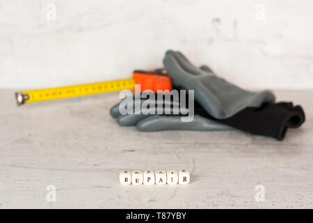 Costruzione nero guanti e un edificio tape sullo sfondo di un muro di cemento. In primo piano l'iscrizione riparazione. Foto Stock
