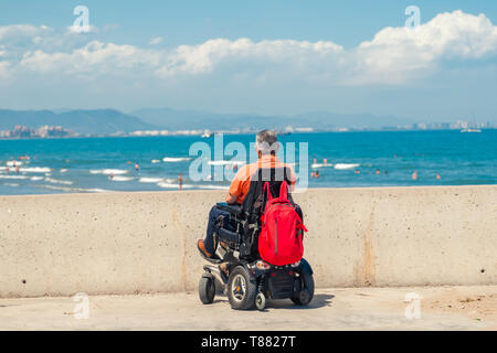 Lonely Man sulla sedia elettrica guardando la spiaggia. La persona disabile in spiaggia. Foto Stock