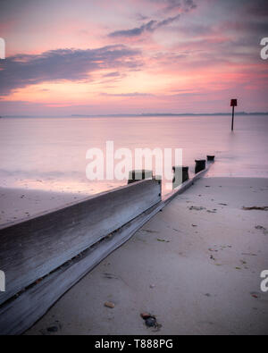 Un mare di legno marcatore o pennelli durante una tranquilla rosa sunrise su di una spiaggia di sabbia Foto Stock