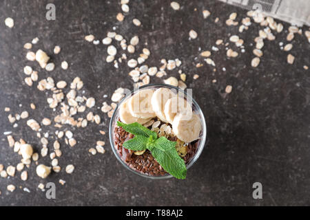 Fiocchi d'avena e gustosi dessert con frutti di bosco freschi, fette di banana e semi di lino in vetro su Tabella grigia Foto Stock