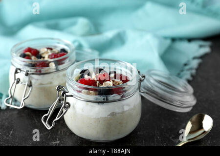 Fiocchi d'avena e gustosi dessert con frutti di bosco freschi in vasetti di vetro sul tavolo Foto Stock