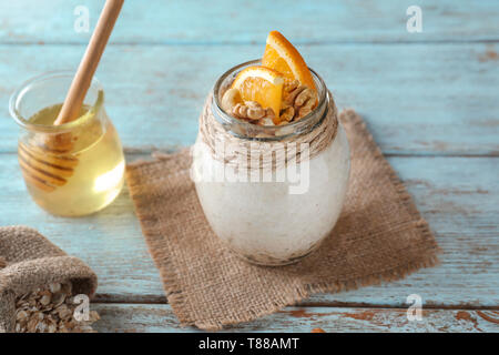 Fiocchi d'avena e gustosi dessert con fette di arancia e noci in un barattolo di vetro su sfondo di legno Foto Stock