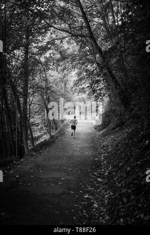 Un lone runner lotte fino la foglia foderato percorso autunnale sulla sponda occidentale del fiume usura sul suo cammino verso il ponte e la Cattedrale. Foto Stock