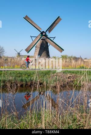 Centro storico di mulini a vento a Kinderdijk, Holland Olanda, un sito Patrimonio Mondiale dell'UNESCO. Ciclo di ciclisti passato in primo piano. Foto Stock