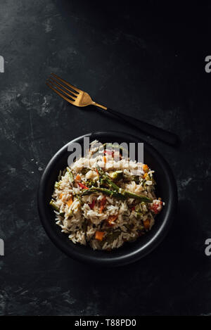 Ciotola con riso basmati con verdure saltati sulla tavola nera Foto Stock