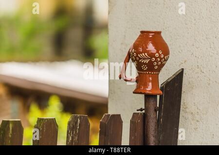 Un vecchio satinato marrone e bianco caraffa messo capovolto su una staccionata di legno accanto al muro bianco di una casa. Sfondo sfocato. La vita rurale nella Repubblica Ceca. Foto Stock