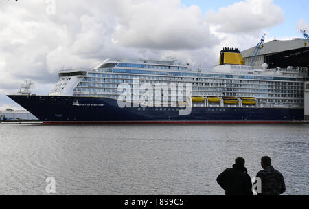 Papenburg (Germania). Il 12 maggio 2019. Due uomini guardare la nave da crociera "spirito di scoperta' lasciando il cantiere navale Meyer Werft la costruzione di dock su una diga. "Lo spirito di scoperta' è 236 metri di lunghezza e poco più di 31 metri di larghezza. Credito: Carmen Jaspersen/dpa/Alamy Live News Foto Stock