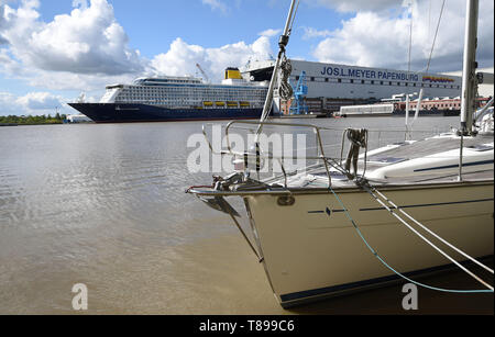 Papenburg (Germania). Il 12 maggio 2019. La nave da crociera "spirito di scoperta' lascia il cantiere navale Meyer Werft la costruzione di dock. In primo piano vi è una barca a vela nell'acqua. "Lo spirito di scoperta' è 236 metri di lunghezza e poco più di 31 metri di larghezza. Credito: Carmen Jaspersen/dpa/Alamy Live News Foto Stock