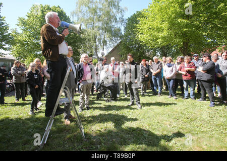 Larz, Germania. Il 12 maggio 2019. Hartmut Lehmann (con Megafon), il sindaco del comune di Lärz, parla in un rally per la conservazione della cultura e della musica festival 'Fusion'. Circa un centinaio di persone hanno protestato domenica in Lärz (Meclemburgo Lake District) contro una stazione di polizia e pattuglie di polizia presso l'alternativa 'Fusion' festival. Credito: dpa picture alliance/Alamy Live News Foto Stock