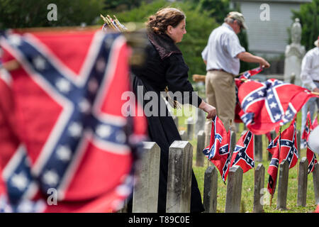 Charleston, STATI UNITI D'AMERICA. 11 Maggio, 2019. Un membro delle Nazioni Figlie della Confederazione, vestito in costume, raccoglie le bandiere di battaglia da grave marker durante il Confederate Memorial Day al Cimitero di magnolia 11 Maggio 2019 a Charleston, Carolina del Sud. Confederate memorial day continua ad essere uno stato ufficiale holiday in Carolina del Sud dove la Guerra Civile Americana ha iniziato a. Credito: Planetpix/Alamy Live News Foto Stock