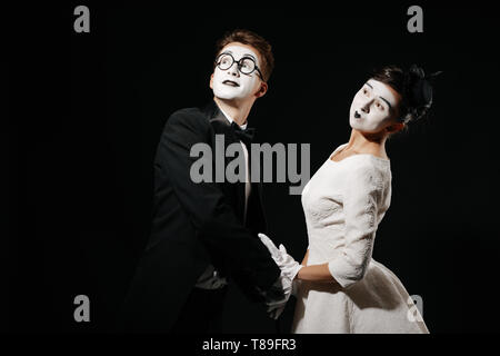 Ritratto di giovane mime su sfondo nero. l uomo in smoking e occhiali e donna in abito bianco Foto Stock