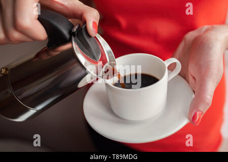 Una donna si versa il caffè in una tazza da una macchina per il caffè. Foto Stock