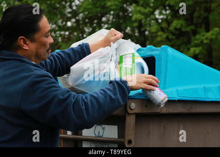 man emptying recyclables into the correct bin in the community dumpster Foto Stock