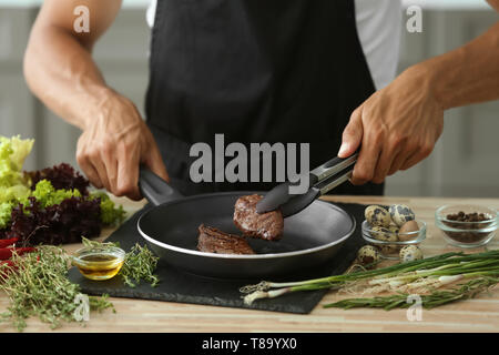 L'uomo prepara deliziosi piatti a base di carne con spezie fresche in cucina Foto Stock