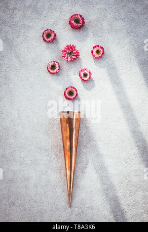 Vintage cono di rame e rosa strawflowers sulla soleggiata sfondo concreto. Foto Stock