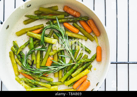 Verdure arrosto, asparagi, la carota e il rosmarino in una padella, vicino, vista dall'alto su sfondo bianco, di cottura, di uno stile di vita sano, Mangiare Sano Foto Stock