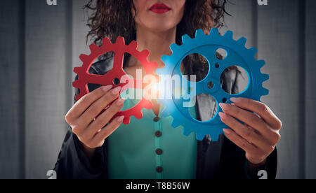 Imprenditrice tenta di collegare pezzi di ingranaggi. Concetto di lavoro di squadra, il partenariato e l'integrazione. Foto Stock