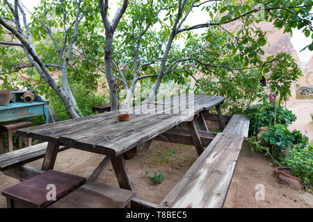 Vecchia sala da pranzo in legno stagionato di tavolo e panche in giardino sotto il mandorlo in attesa per i suoi proprietari Foto Stock