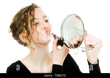 Ragazza adolescente in abito nero facendo fare fino a specchio rotondo - grimace di rossetto - sfondo bianco Foto Stock