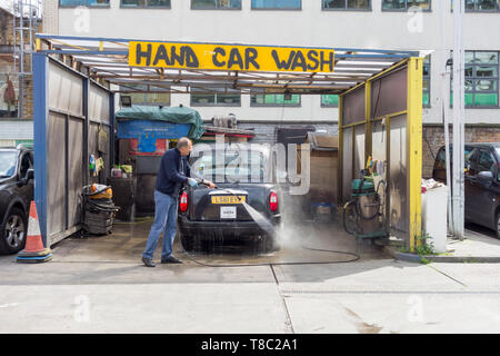 Un uomo che lava un taxi nero di Londra in un autolavaggio a Southwark, Londra, Inghilterra, Regno Unito Foto Stock