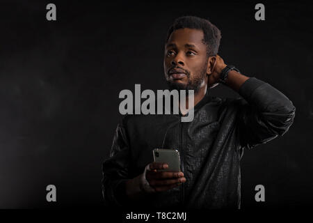 Piscina colpo di colpiti e stupiti attraente African American uomo con barba e capelli corti, tenendo lo smartphone, guardando sorpreso gadget scre Foto Stock