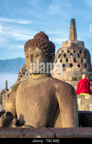 Statua di Buddha con un monaco buddista pregando nel retro, tempio di Borobudur complessa, il Borobudur, Yogyakarta, Java, Indonesia Foto Stock