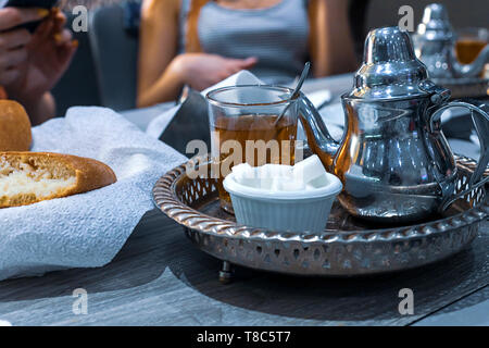 Tè marocchino con la menta e lo zucchero in una occhiali su una piastra di rame con bollitore. Il Marocco Foto Stock