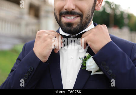 Bel giovane sposo che fissa il filtro bow tie all'aperto, primo piano Foto Stock