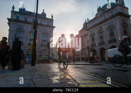 Un ciclista attraverso cicli di Piccadilly Circus a Londra come il sole tramonta in una sera d'estate - insolitamente, nessun auto o autobus a tutti Foto Stock